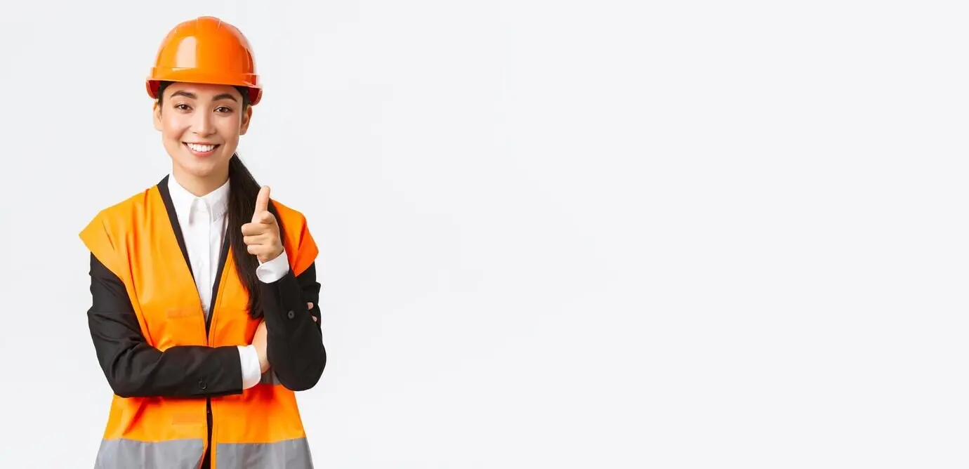Erfolgreiche, selbstbewusste, lächelnde asiatische Architektin; zeigt mit dem Finger auf die Kamera; trägt Sicherheitshelm und reflektierende Jacke; stellt ein Bauprojekt vor; industrielle Frau, die Kunden einlädt.